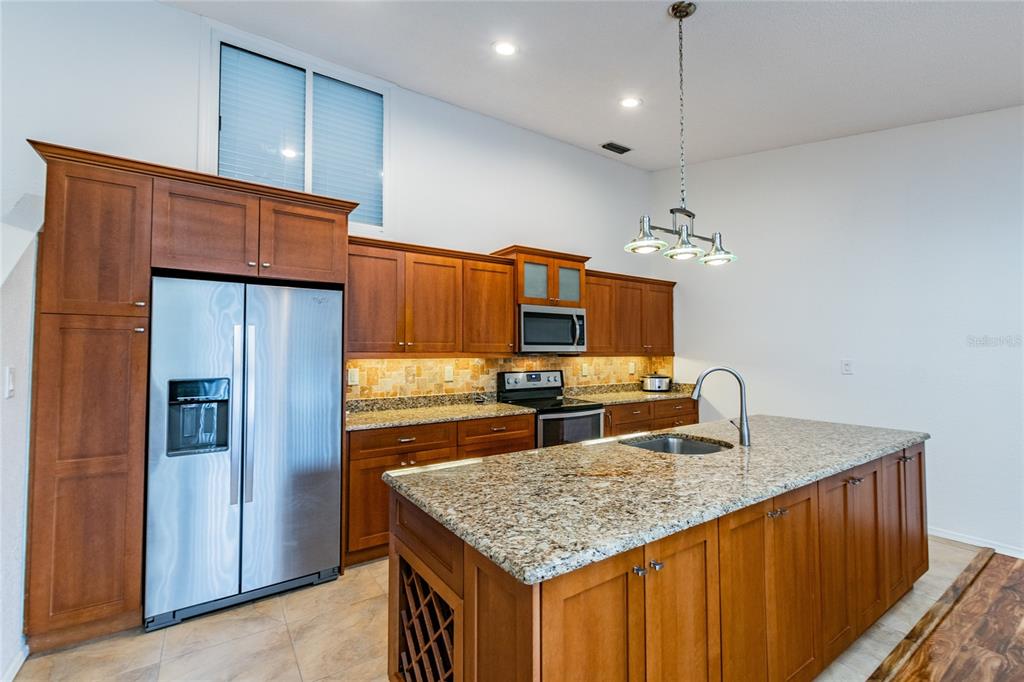 A kitchen features wood cabinets, granite countertops, a stainless steel refrigerator, and a center island — 6435 92ND PLACE UNIT 904, PINELLAS PARK, FL