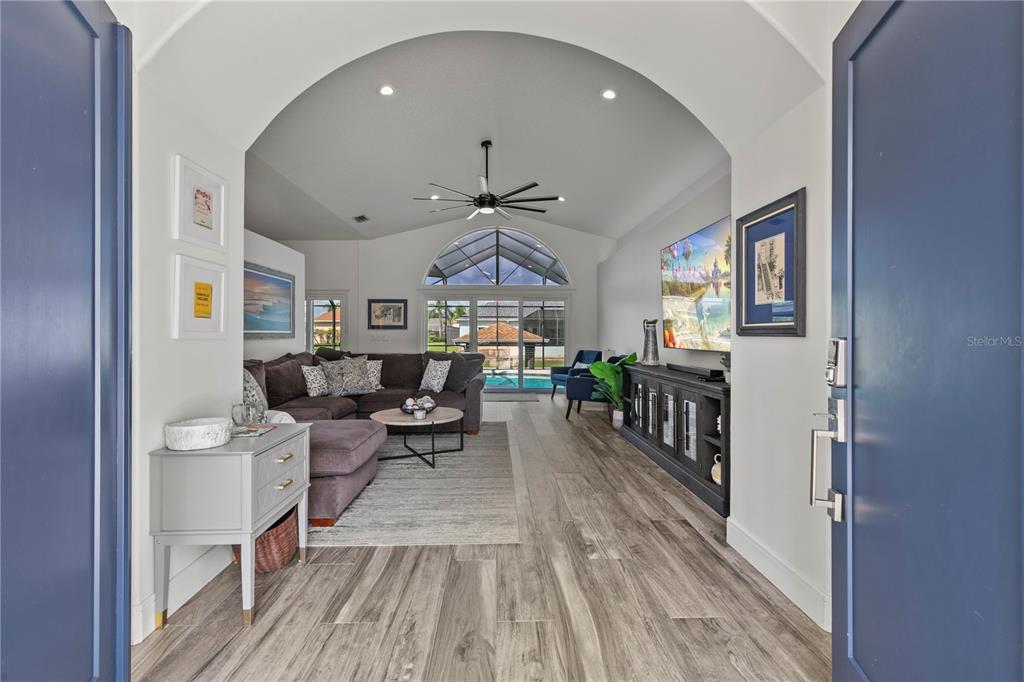 A living room with wood-look flooring, a vaulted ceiling, and a view of a pool — 17 COLLINGTON COURT, PALM COAST, FL