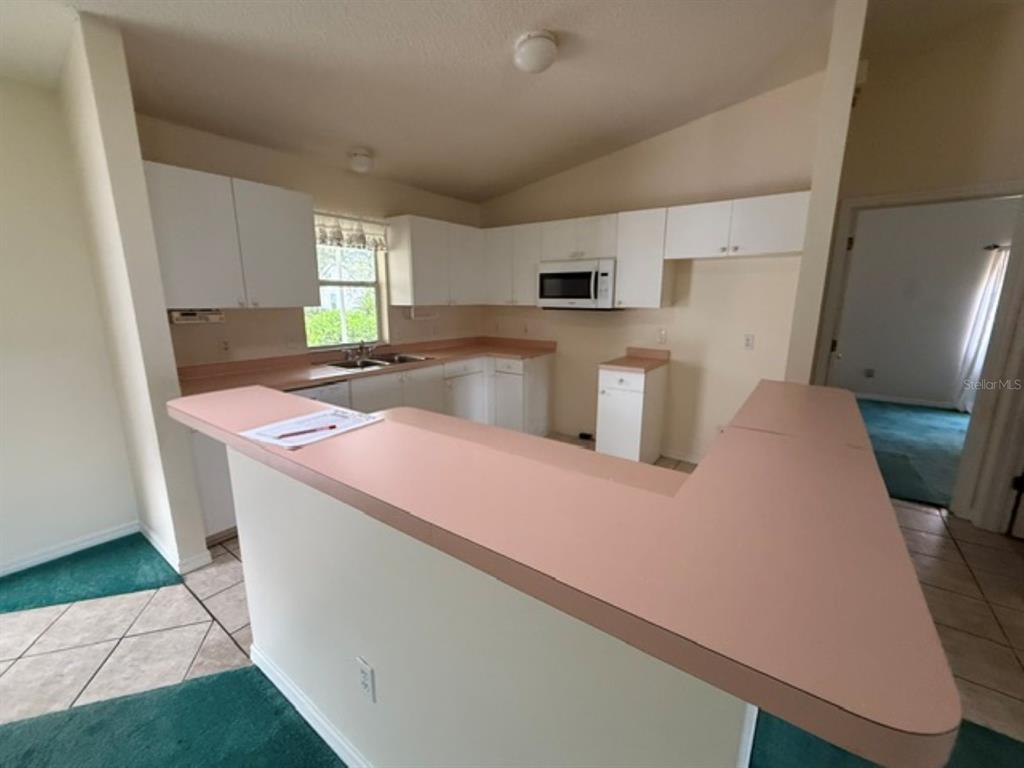 A kitchen features white cabinets, pink countertops, a breakfast bar, and a window — 208 ARAGON LANE, LADY LAKE, FL