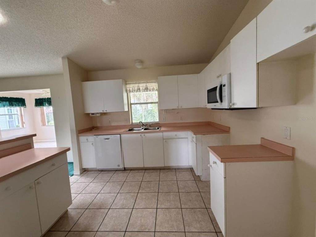 A kitchen with white cabinets, pink countertops, and light-colored tile flooring — 208 ARAGON LANE, LADY LAKE, FL