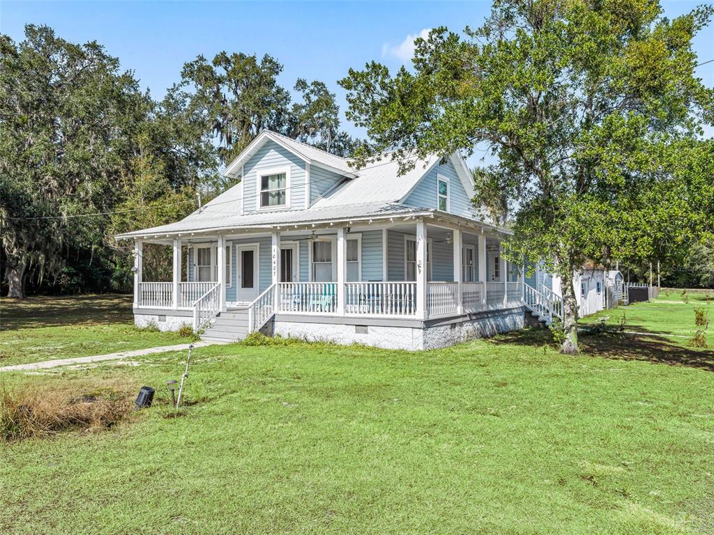 A light blue, two-story farmhouse with a wraparound porch sits on a grassy lot — 10487 SE HIGHWAY 42, SUMMERFIELD, FL