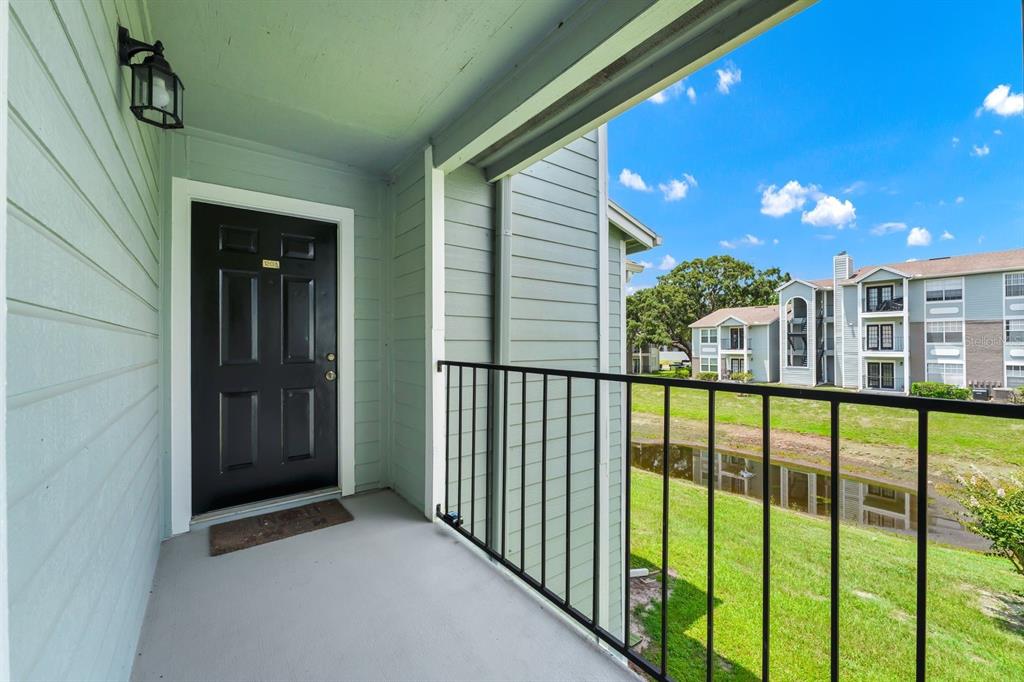 A balcony with a black door, metal railing, and a view of a grassy pond area — 2550 N ALAFAYA TRAIL UNIT 1203, ORLANDO, FL