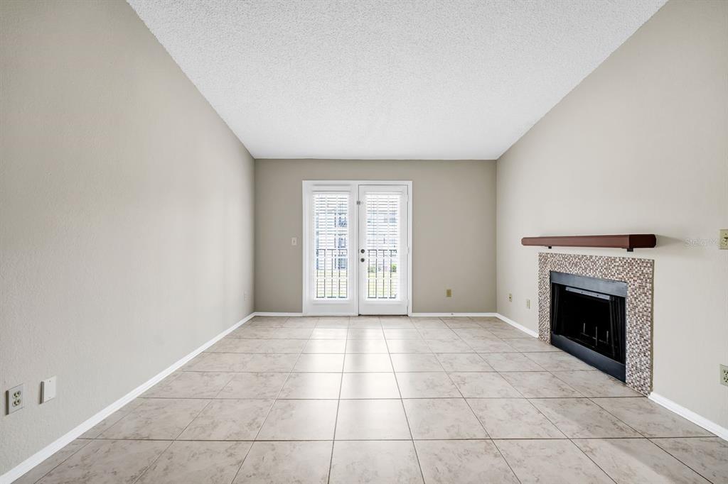 An empty living room features beige tile flooring, a fireplace with a mantel, and glass doors — 2550 N ALAFAYA TRAIL UNIT 1203, ORLANDO, FL