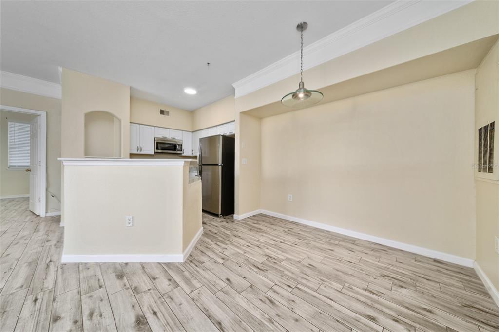 A kitchen with white cabinets and stainless steel appliances opens to a dining area — 3280 SOHO STREET UNIT 201, ORLANDO, FL