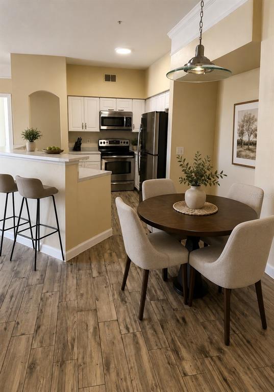 A kitchen with white cabinets and stainless steel appliances sits beside a small dining area — 3280 SOHO STREET UNIT 201, ORLANDO, FL