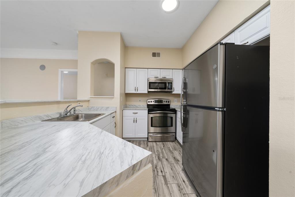 A kitchen features white cabinets, stainless steel appliances, and a marble-patterned countertop — 3280 SOHO STREET UNIT 201, ORLANDO, FL