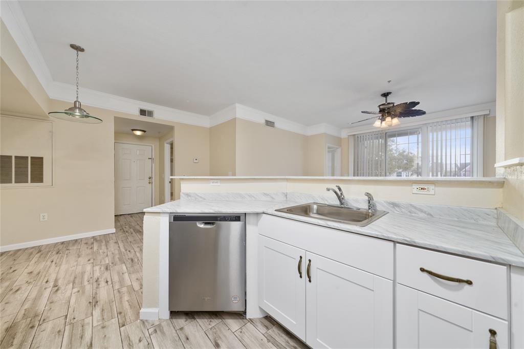 A kitchen features white cabinets, marble-look countertops, stainless steel appliances, and wood-look tile flooring — 3280 SOHO STREET UNIT 201, ORLANDO, FL