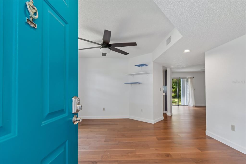 An open teal door reveals a living area with wood floors, a ceiling fan, and shelves — 11800 PARK BOULEVARD UNIT 401, SEMINOLE, FL