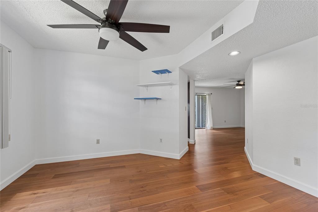 An empty room with hardwood floors, a ceiling fan, and floating shelves on the wall — 11800 PARK BOULEVARD UNIT 401, SEMINOLE, FL