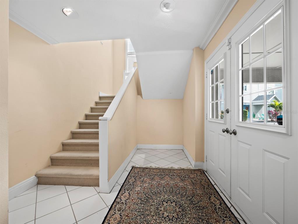 An entryway features a carpeted staircase, white tile flooring, a patterned rug, and a front door — 836 EVERGREEN WAY, LONGBOAT KEY, FL