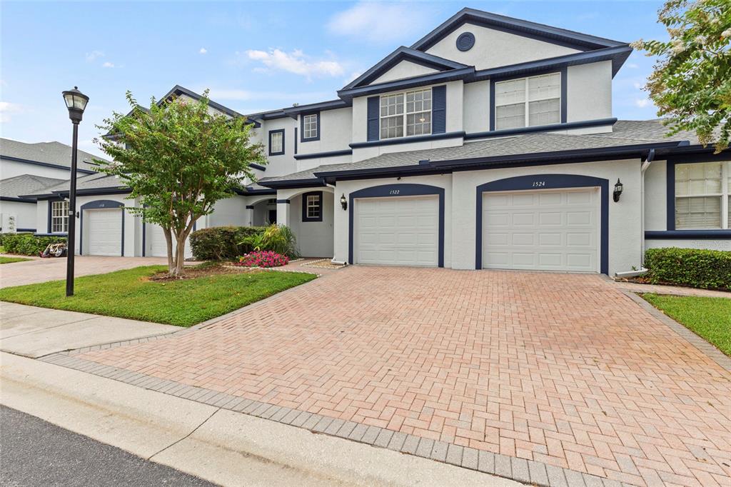 A two-story townhouse exterior features a brick paver driveway, two garage doors, and light-colored siding — 1522 SUMMERGATE DRIVE, VALRICO, FL
