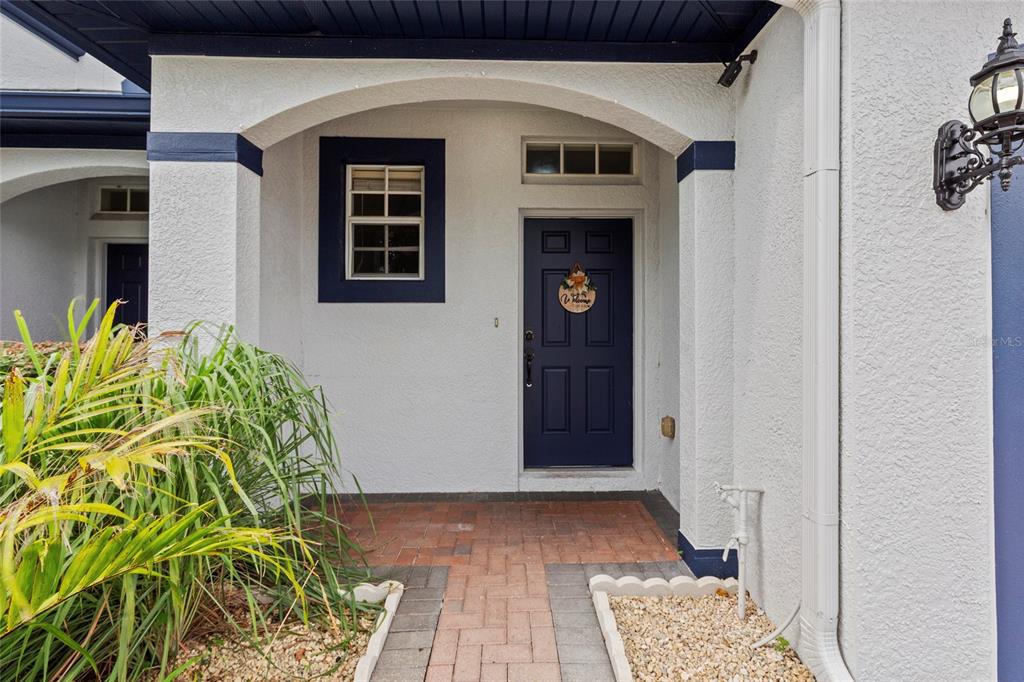 A covered entryway features a dark blue front door, a brick walkway, and stucco walls — 1522 SUMMERGATE DRIVE, VALRICO, FL