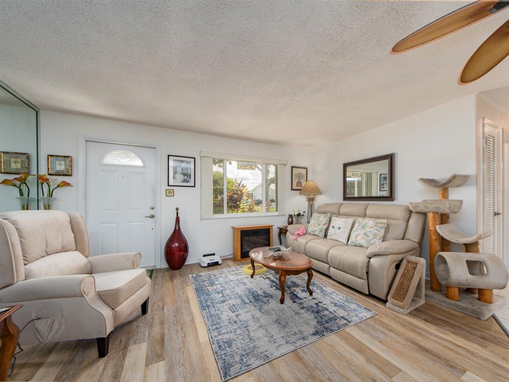 A living room features light wood-look flooring, a beige sofa, an armchair, and a cat tree — 14104 89TH AVENUE, SEMINOLE, FL