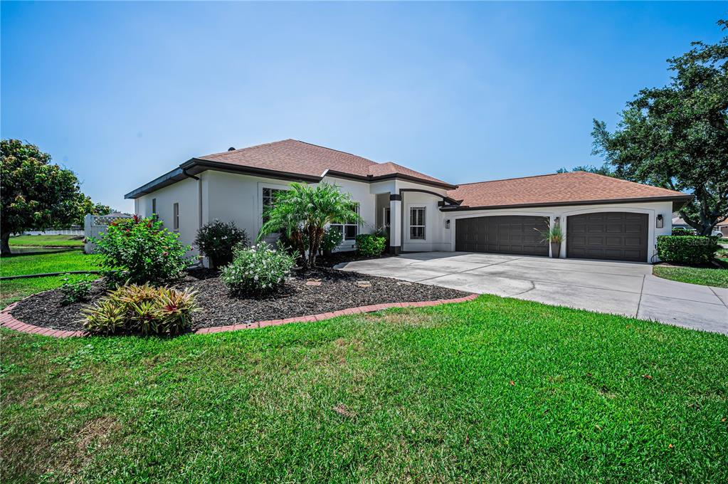 A single-story house with a tan exterior, a three-car garage, and a landscaped front yard — 11423 30TH COVE E, PARRISH, FL