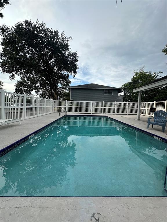 A rectangular swimming pool sits in a fenced backyard with a grey house in the background — 1910 W SLIGH AVENUE UNIT E102, TAMPA, FL