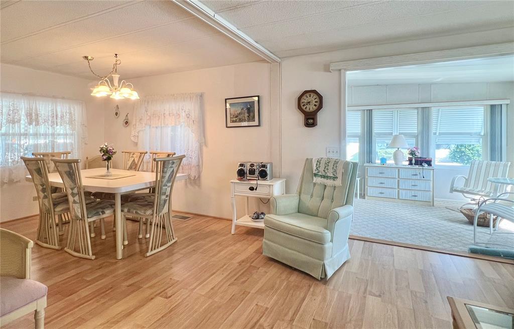 A dining area with wood-look flooring flows into a carpeted sunroom featuring a light-green armchair — 1100 BELCHER ROAD S UNIT 197, LARGO, FL