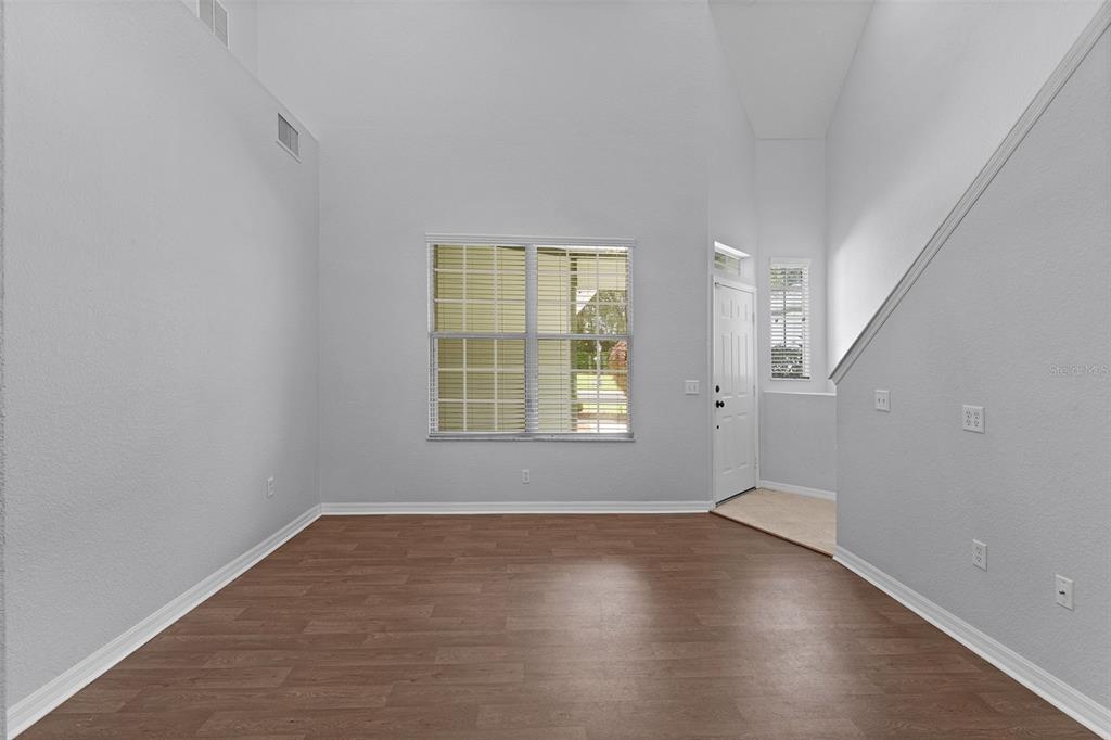 An empty room with high ceilings, light gray walls, and wood-look flooring features a window — 231 NE 28TH AVENUE UNIT 103, OCALA, FL
