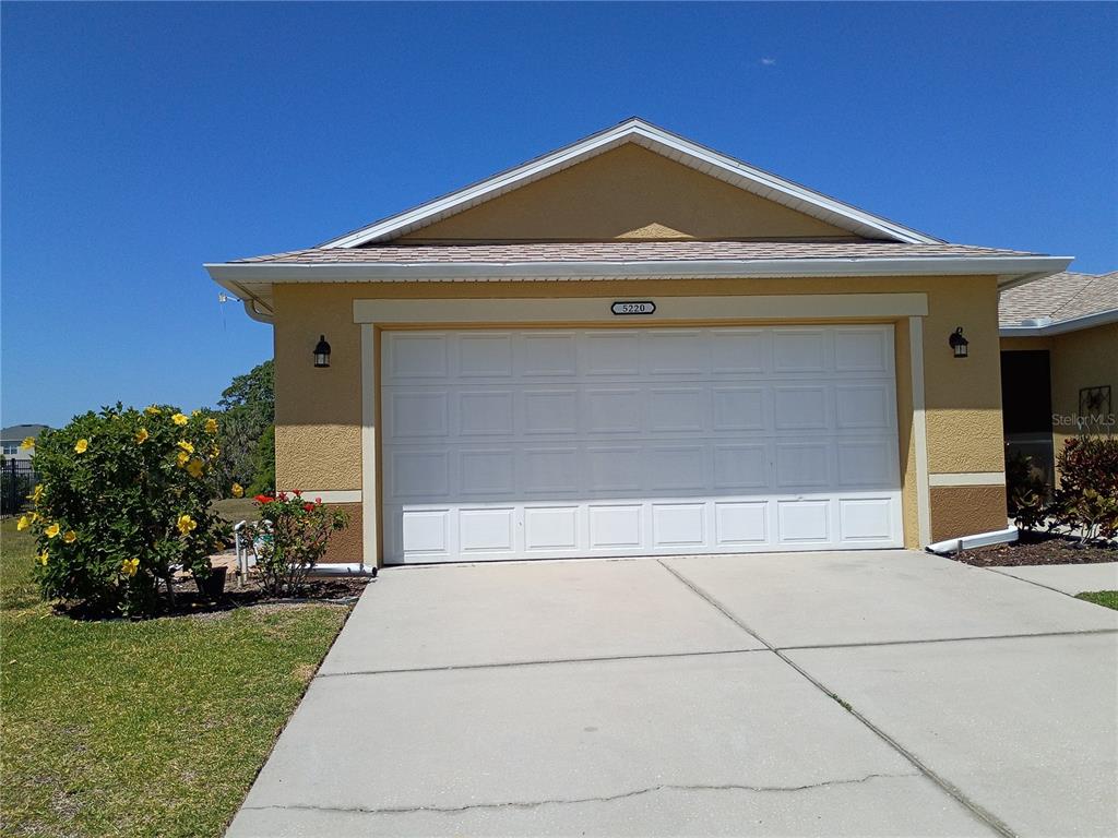 A single-story house exterior features a two-car garage, yellow stucco walls, and a concrete driveway — 5220 BUTTERFLY SHELL DRIVE, APOLLO BEACH, FL