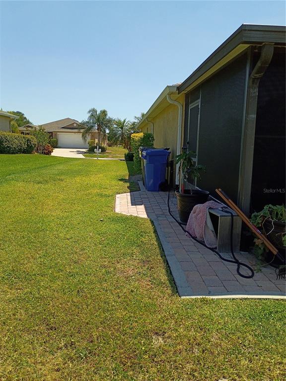 A paved patio area sits beside a house with a screened-in porch and lawn — 5220 BUTTERFLY SHELL DRIVE, APOLLO BEACH, FL