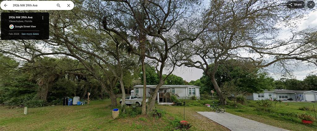 A single-story manufactured home sits on a grassy lot shaded by several large trees — 3926 NW 39TH AVENUE, OKEECHOBEE, FL