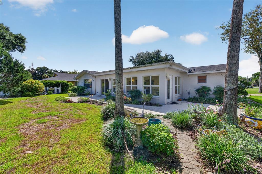 The exterior of a single-story house features a concrete patio, landscaping, and two tall trees — 802 SANDWEDGE DRIVE, NEW SMYRNA BEACH, FL