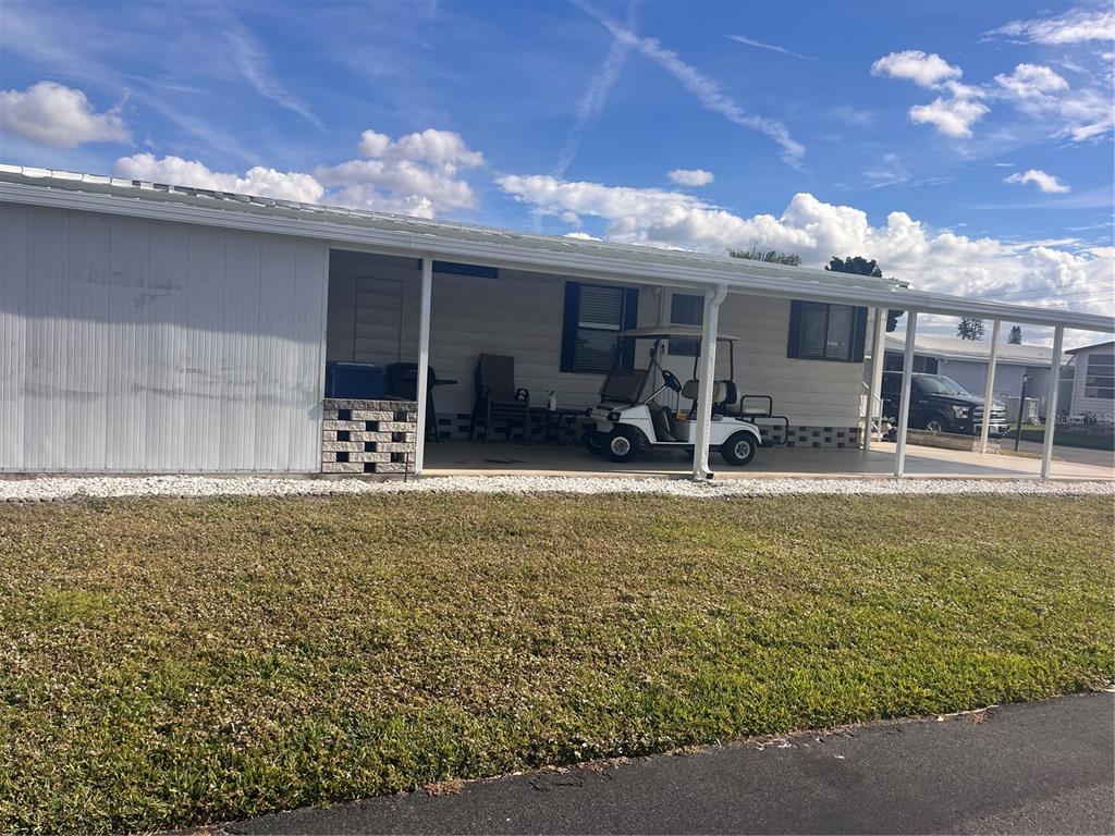 A single-story manufactured home features a covered carport with a golf cart parked underneath — 5316 53RD AVENUE E UNIT M15, BRADENTON, FL