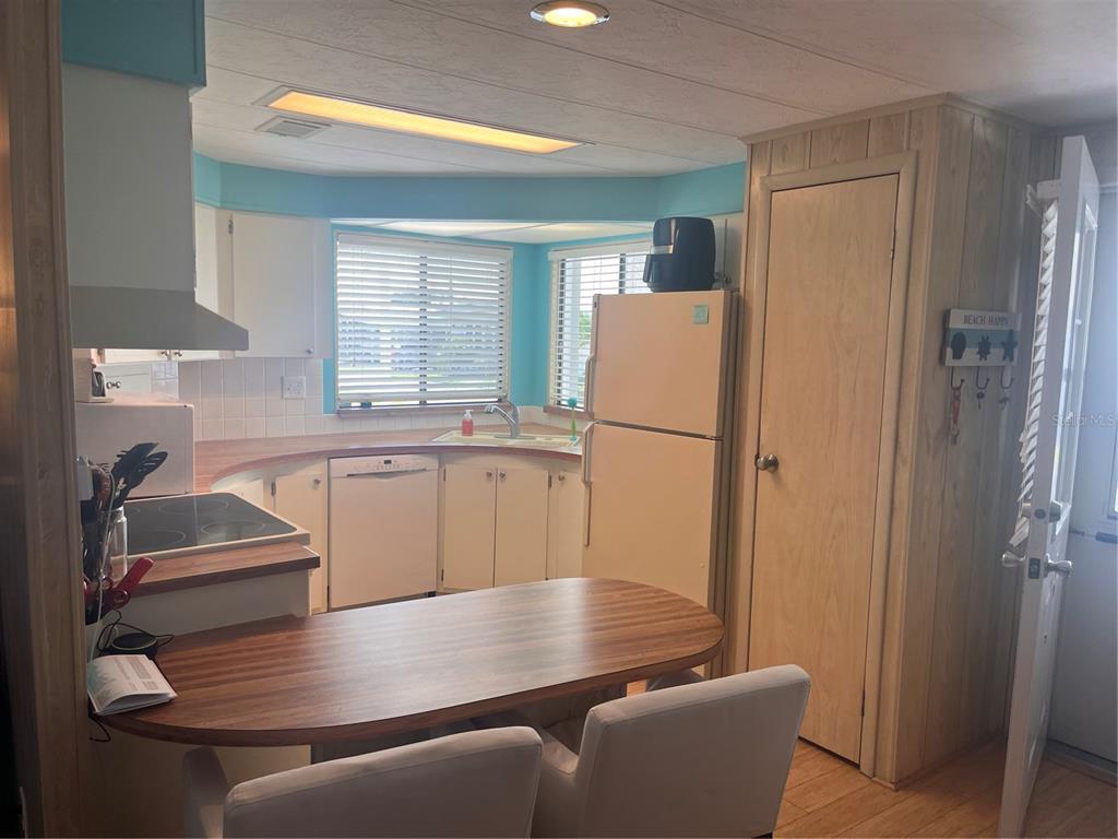 A kitchen features a curved wooden breakfast bar, white cabinets, and light wood-paneled walls — 5316 53RD AVENUE E UNIT M15, BRADENTON, FL
