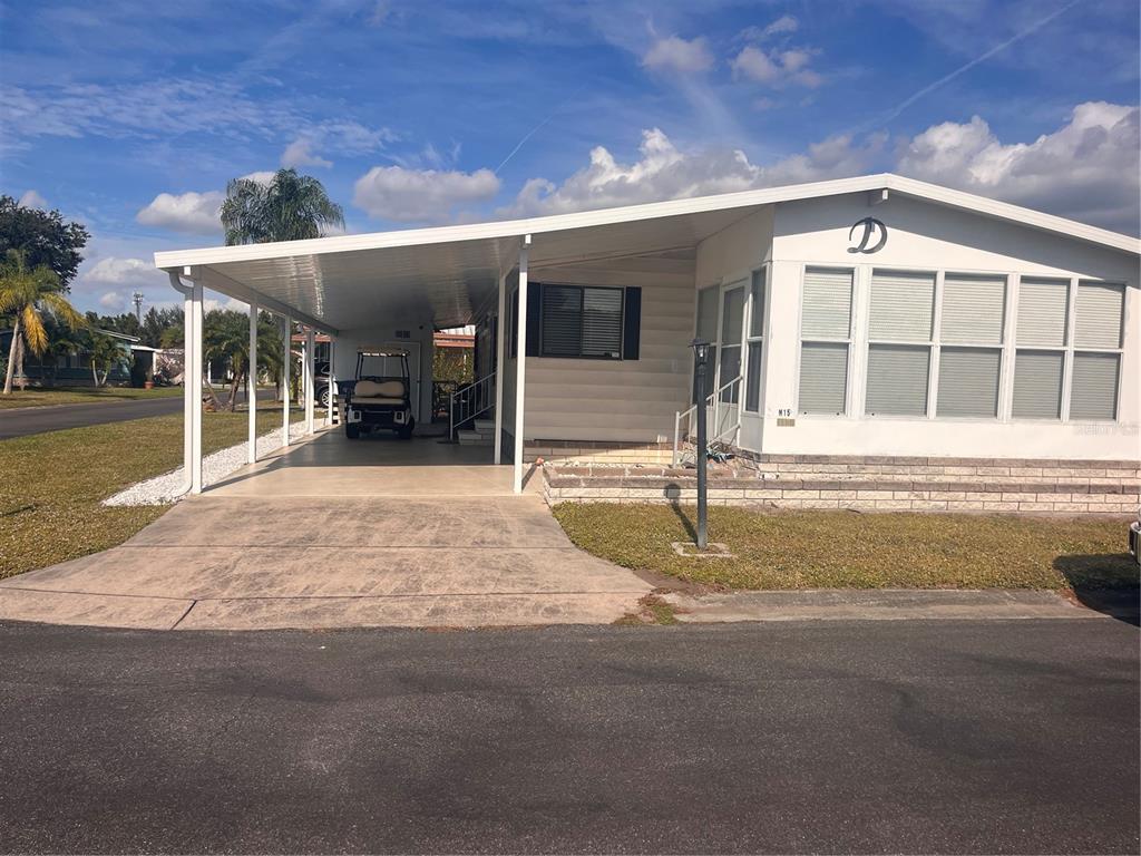 A single-story manufactured home with a carport, a golf cart, and a brick-accented front porch — 5316 53RD AVENUE E UNIT M15, BRADENTON, FL