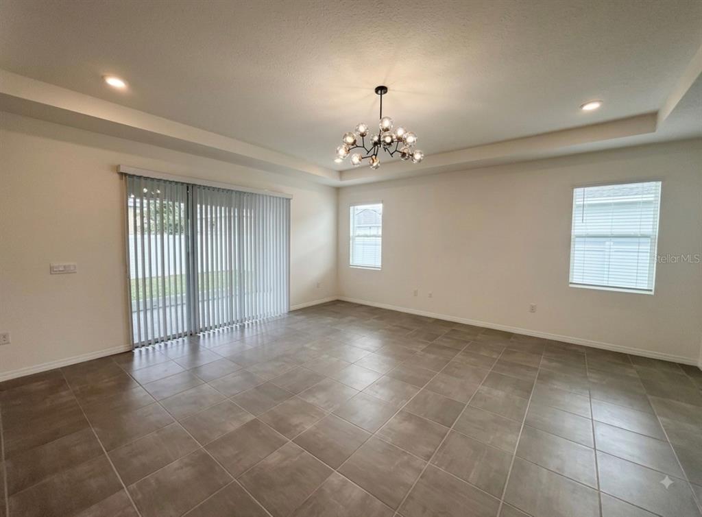 An empty room features large floor tiles, a tray ceiling, a chandelier, and sliding glass doors — 5811 SW 80TH LANE, OCALA, FL