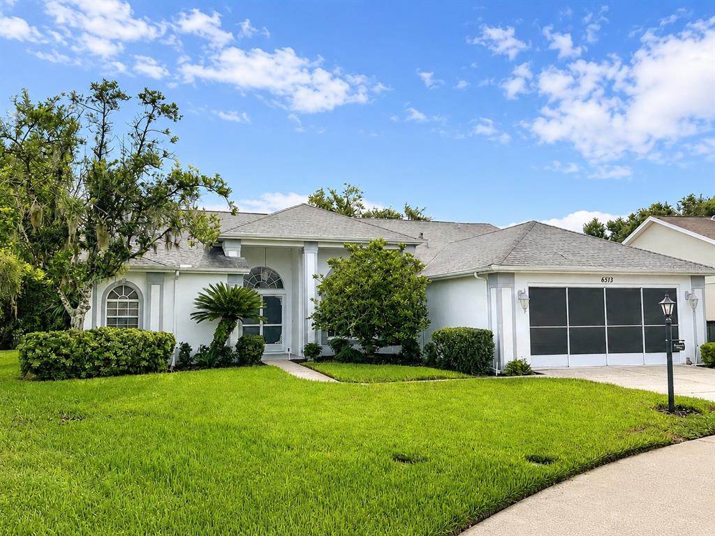 A single-story house with a white exterior, a screened garage, and a landscaped front lawn — 6513 CARDINAL CREST DRIVE, NEW PORT RICHEY, FL