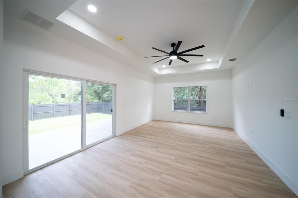 An empty room with light wood floors, a tray ceiling, a ceiling fan, and sliding doors — 6308 NOTRE DAME TERRACE, NORTH PORT, FL