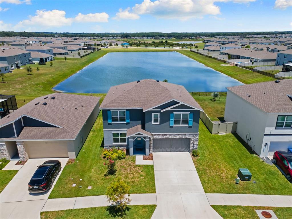 An aerial view of a two-story suburban house with a blue exterior and lakefront backyard — 9728 CRESCENT RAY DRIVE, WESLEY CHAPEL, FL