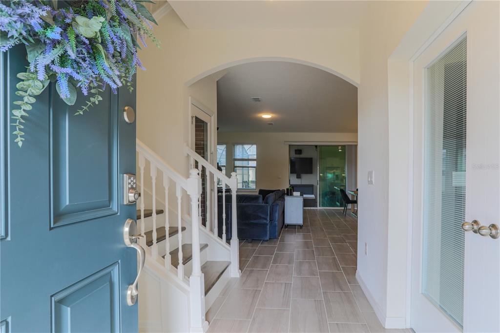 An entryway with a blue door, white staircase, and tile flooring leads to a living area — 16625 POINT ROCK DRIVE, WINTER GARDEN, FL