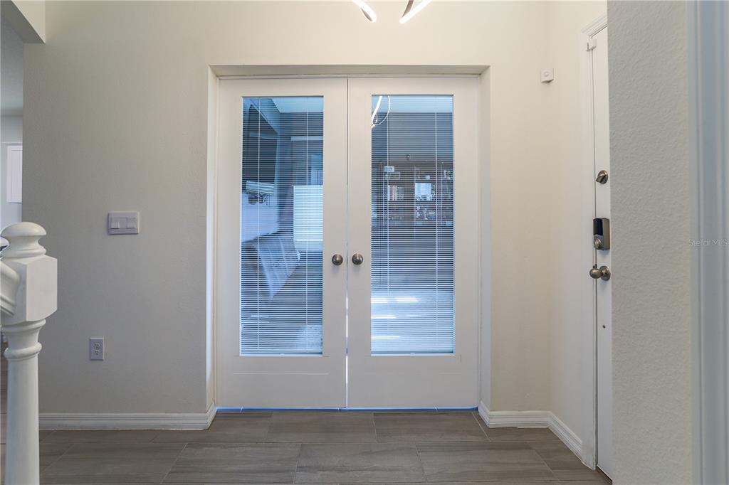 A foyer features white double French doors with integrated blinds and gray tile flooring — 16625 POINT ROCK DRIVE, WINTER GARDEN, FL