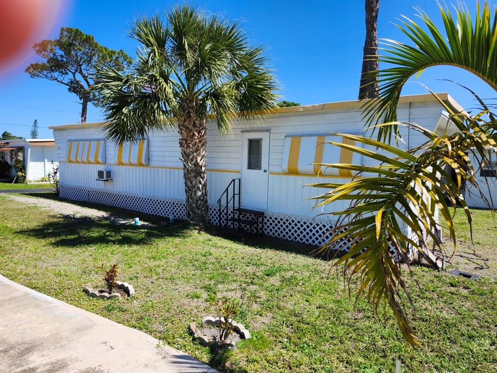 A white mobile home with yellow trim and lattice skirting sits on a grassy lot — 12674 SEMINOLE BOULEVARD UNIT C30, LARGO, FL