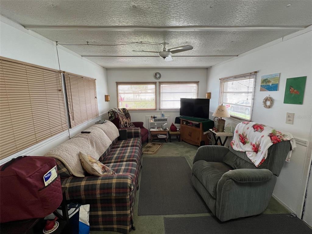 A living room features a plaid sofa, a green recliner, a television, and window blinds — 12674 SEMINOLE BOULEVARD UNIT C30, LARGO, FL