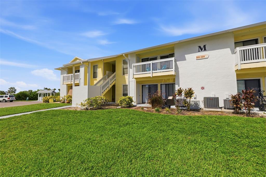 A two-story apartment building with yellow siding, white balconies, and a grassy front lawn — 455 ALT 19 S UNIT 218, PALM HARBOR, FL