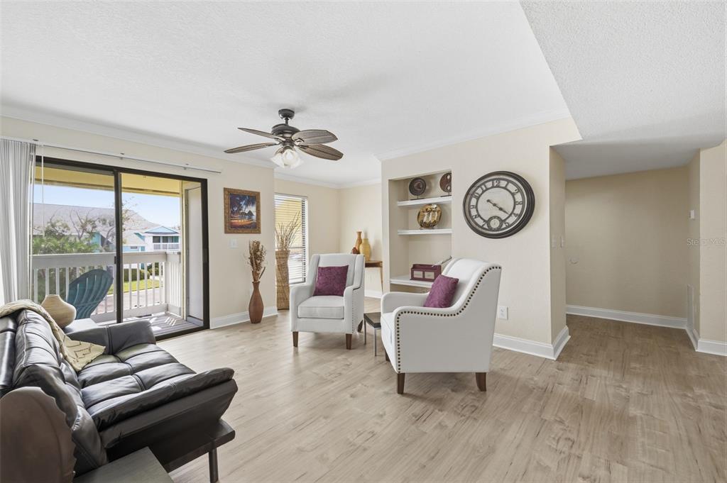 A living room with light wood flooring, two white armchairs, a dark sofa, and built-in shelving — 455 ALT 19 S UNIT 218, PALM HARBOR, FL