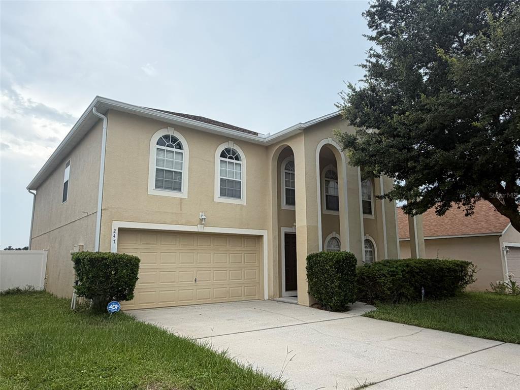 A two-story tan stucco house features an attached garage and an arched entryway — 247 BLAKE AVENUE, DAVENPORT, FL