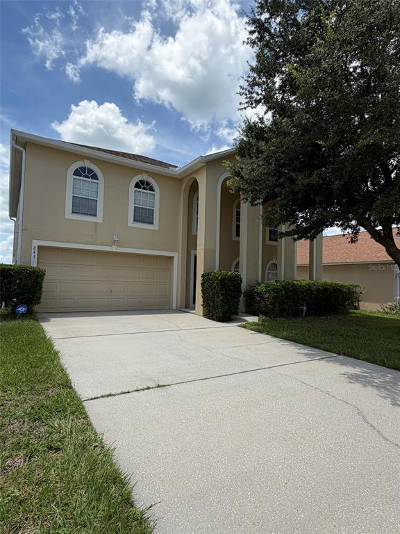 A two-story beige house with a two-car garage and a large tree in front — 247 BLAKE AVENUE, DAVENPORT, FL