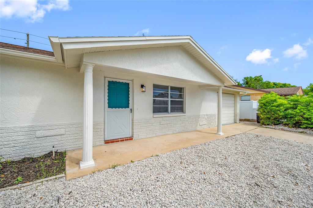 The exterior of a single-story house features a covered porch, white columns, and gravel landscaping — 11724 PAIGE DRIVE, PORT RICHEY, FL