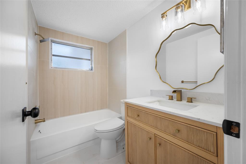 A bathroom features a wood vanity, a scalloped mirror, and a tiled tub-shower combination — 11724 PAIGE DRIVE, PORT RICHEY, FL
