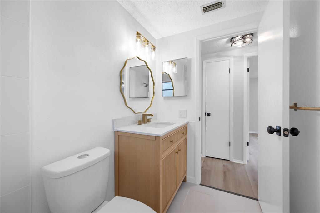 A bathroom features a light wood vanity, gold-rimmed mirror, white toilet, and white walls — 11724 PAIGE DRIVE, PORT RICHEY, FL