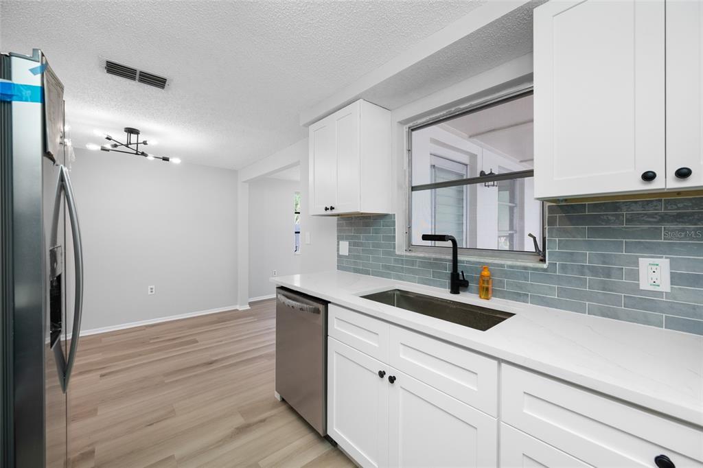 A kitchen features white cabinets, a stainless steel dishwasher, and a blue subway tile backsplash — 11724 PAIGE DRIVE, PORT RICHEY, FL