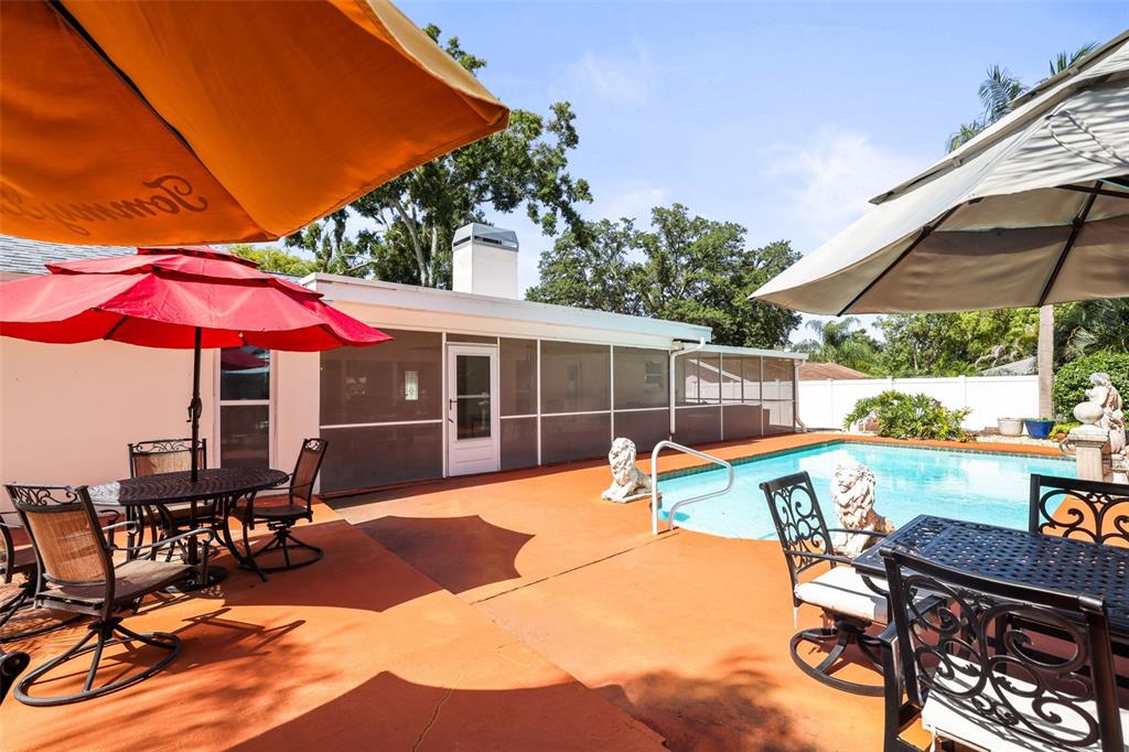 A backyard patio features a swimming pool, two patio tables with umbrellas, and screen enclosures — 1981 CASTILLE DRIVE, DUNEDIN, FL