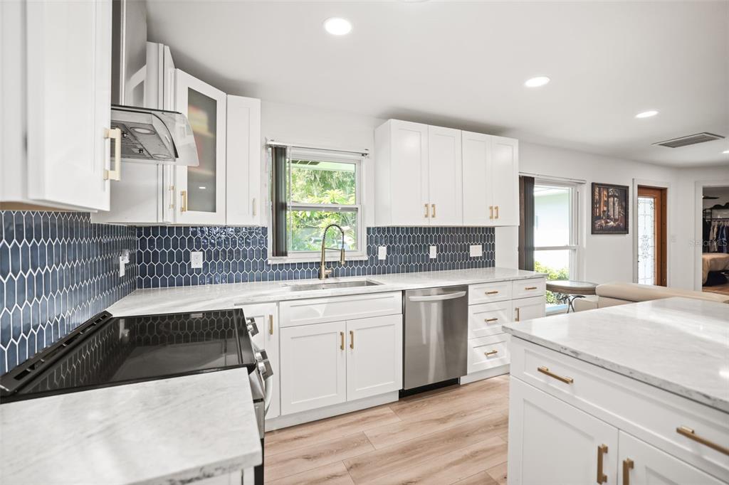 A modern kitchen features white cabinets, blue picket-tile backsplash, stainless steel appliances, and marble countertops — 1981 CASTILLE DRIVE, DUNEDIN, FL