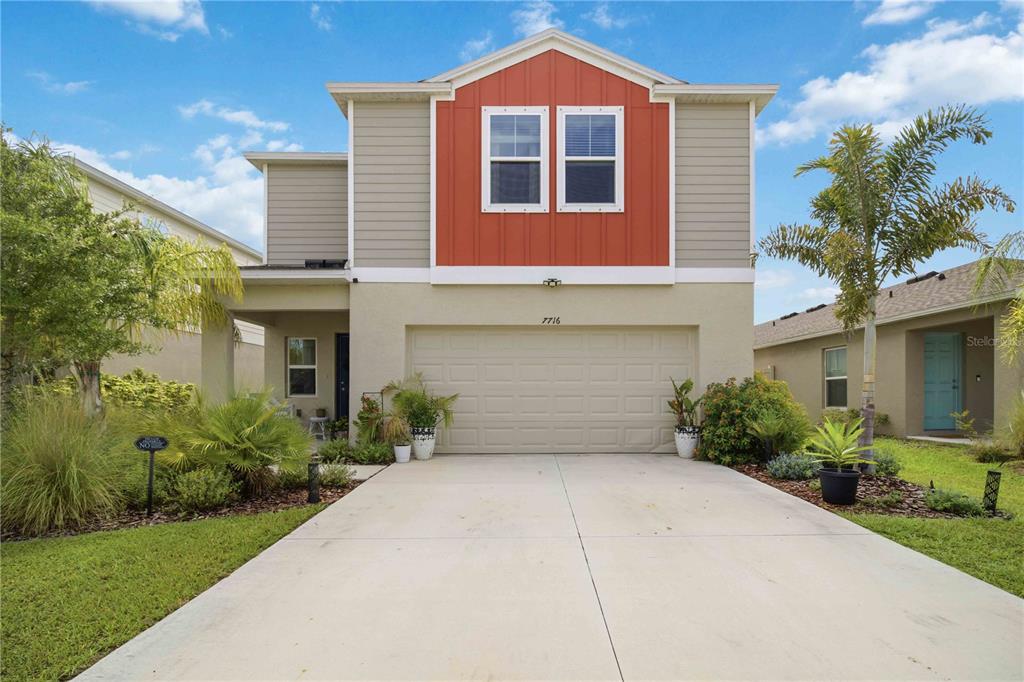 A two-story house with a beige stucco garage, tan siding, and a red-accented upper gable — 7716 TWINLEAF TERRACE, PARRISH, FL