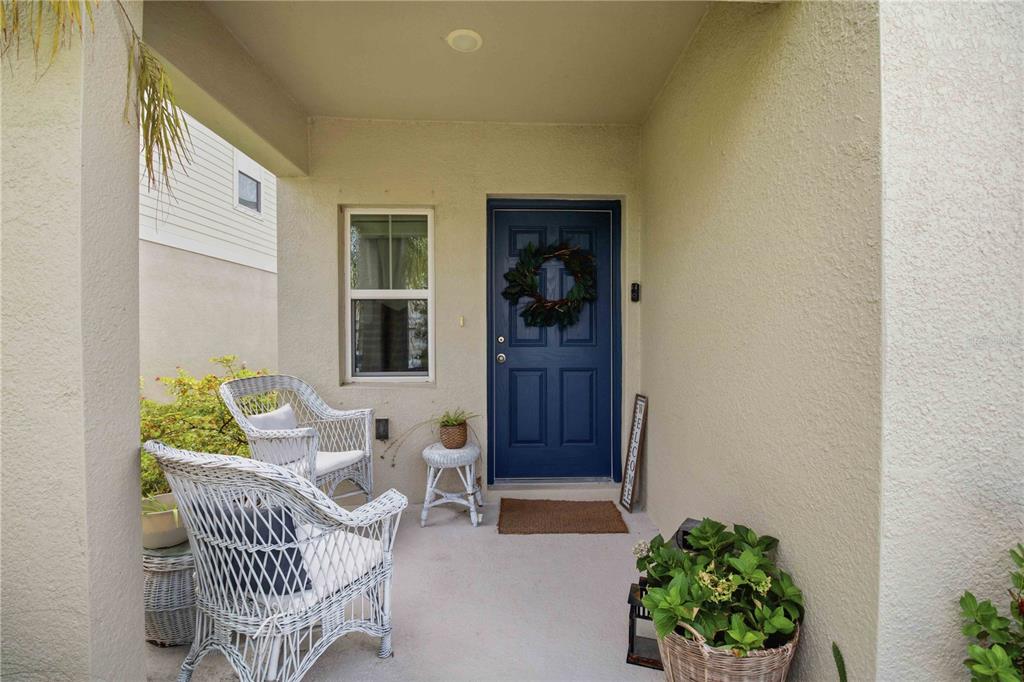 A covered front porch features two white wicker chairs, a blue door, and potted plants — 7716 TWINLEAF TERRACE, PARRISH, FL