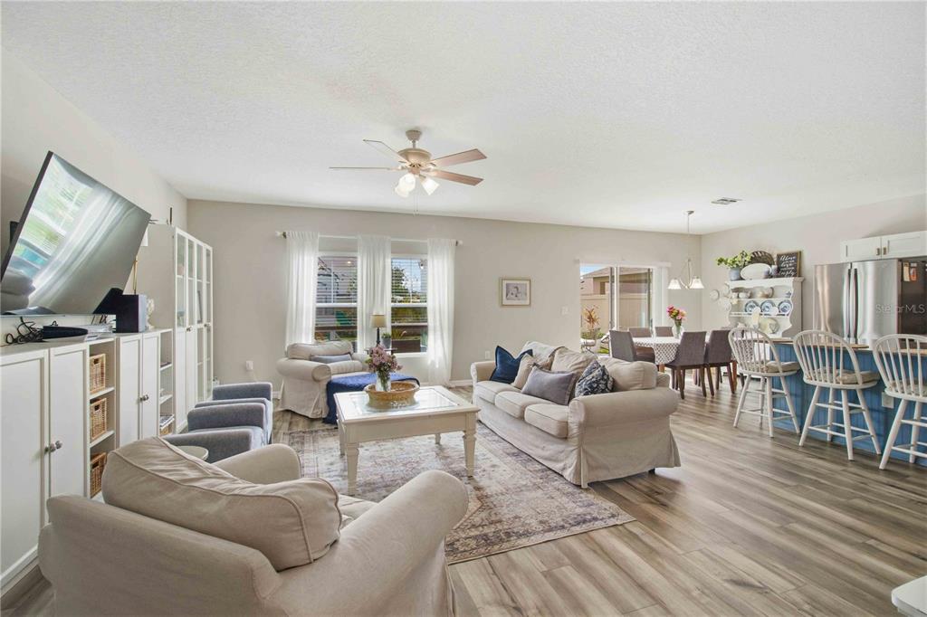 An open-concept living and dining area features light wood flooring, neutral furniture, and a kitchen — 7716 TWINLEAF TERRACE, PARRISH, FL