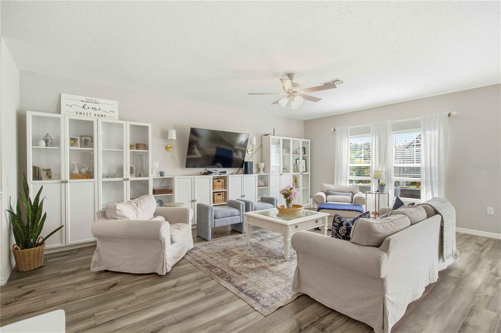 A bright living room features white cabinetry, a large television, and light wood-look flooring — 7716 TWINLEAF TERRACE, PARRISH, FL